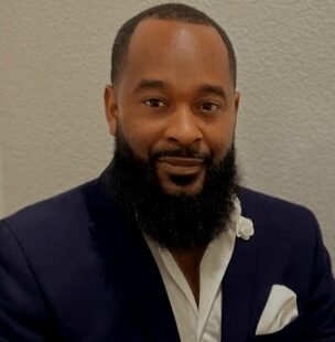 Man in suit with beard, smiling gently.